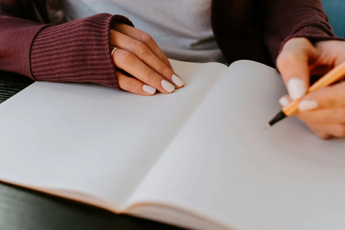 Hands writing a goal in an open notebook